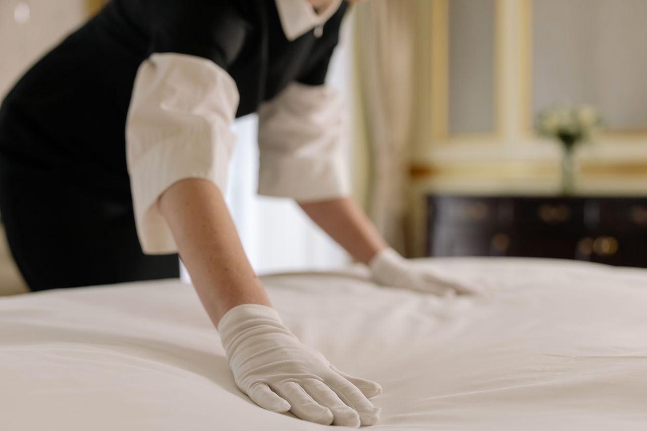 services-01 A housekeeper straightening the bed linens in a well-appointed hotel room.